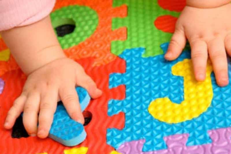 Mani di bambino piccolo che giocano con un puzzle.
